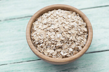 Raw Oat flakes in a wooden bowl on a green background. Ingredient for cooking. Close up, selective focus
