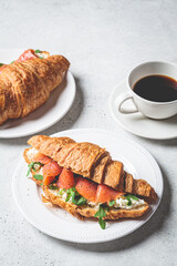 Croissant sandwich with cream cheese, salmon and arugula on white plate, gray background. Healthy breakfast concept.
