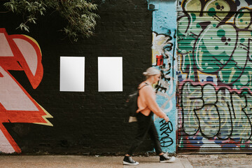 Woman walking past street art mural and blank posters - Powered by Adobe