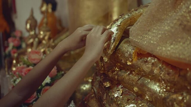 Hand of buddhist girl apply gold leaf to buddha statue.