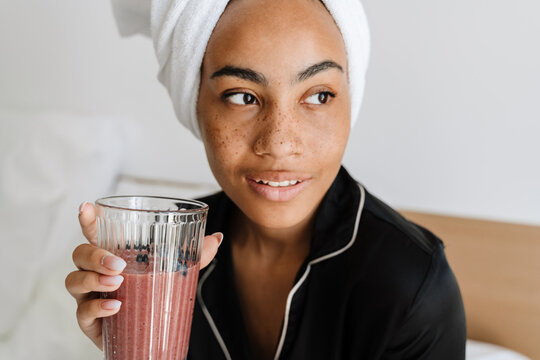 Young Black Woman Drinking Smoothie While Sitting At Bedroom