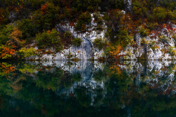 turquoise blue mountain lake with reflections of cliffs and forest in intense fall colors