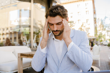 Young man with headache rubbing his temples while sitting at cafe