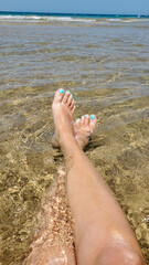Close-up of women's legs sunbathing on the shore of the turquoise sea on a sunny day