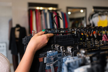 female hand sorting through hangers with jeans in a store, women's clothing on racks, a choice of trousers in a boutique.