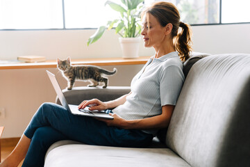 Ginger mature woman typing on laptop while sitting on couch