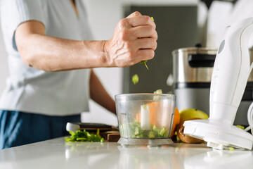 White mature woman cooking with blender in kitchen