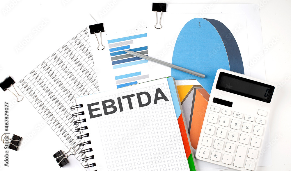 Poster text ebitda on a notebook on the diagram and charts with calculator and pen