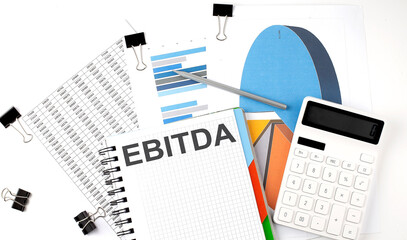 Text EBITDA on a notebook on the diagram and charts with calculator and pen