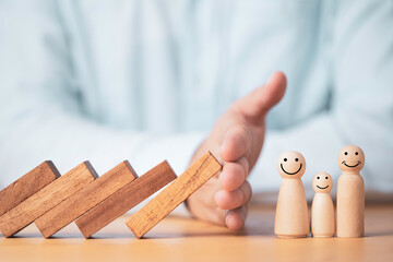 Businessman hand gesture protecting wooden domino falling to family dolls for insurance and...