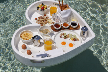 Fototapeta na wymiar White heart shaped floating tray. Breakfast in pool in luxury resort. Top view. 