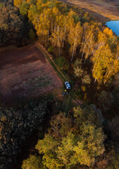 Aerial view of lake at sunrise in autumn. Vertical photo, orange grass, trees at dawn. Colorful aerial landscape of river coast at sunset in fall. Leisure and hobbies. A park. car and people