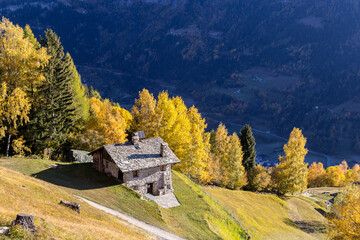 Cadera, Switzerland - October 28. 2021: A stone cottage in Village Cadera on the Alps mountain slope over the Puschlav Valley in colorful autumn season, Grison, Switzerland