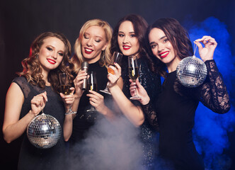 Group of partying girls clinking flutes with sparkling wine and holding disco balls and microphone.