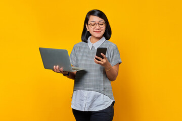 Portrait of beautiful smiling Asian woman holding laptop and cell phone on blue background