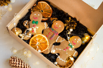 Christmas gingerbread men in an eco-friendly gift box with dried oranges, garland and bokeh. Christmas holiday background, gifts, top view