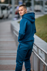 A young man in a tracksuit stands in a city park