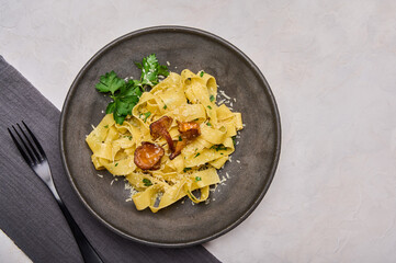 Homemade pasta pappardelle with mushrooms chanterelles, cheese and parsley on dark plate with black fork and napkin, top view