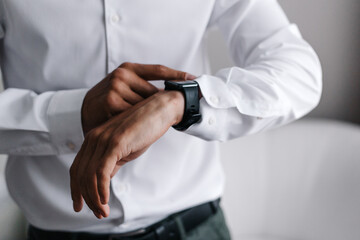 Fototapeta na wymiar A business man in a white shirt, using a smartwatch. Man's hands close up.