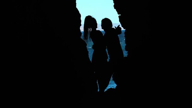 Black silhouette of a straight couple hugging in the entry to the sea cave