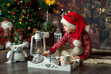 Cute toddler child, boy in a christmas outfut, playing in a wooden cabin on Christmas, derocation around him