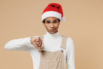 Young disappointed sad african man 20s wear Santa Claus red Christmas hat show thumb down dislike...