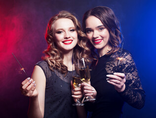Two beautiful young women in black dress with wine glasses and sparkles.