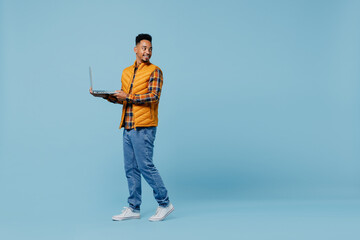 Full size body length happy young black man 20s years old wear yellow waistcoat shirt hold use work on laptop pc computer looking behind isolated on plain pastel light blue background studio portrait