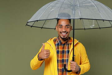 Young black man 20s years old wears yellow raintcoat shirt hold umbrella show thumb up like gesture...