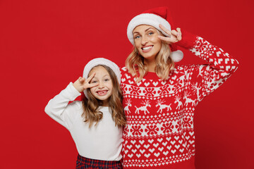 Young woman in sweater have fun with child baby girl 6-7 years old. Mommy little kid daughter show victory v-sign gesture isolated on plain red color background studio. New Year love family concept.