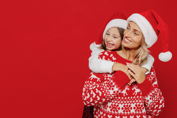 Young minded dreamful woman in sweater hat have fun with child baby girl 6-7 years old. Mommy little kid daughter look aside isolated on plain red color background studio New Year love family concept.