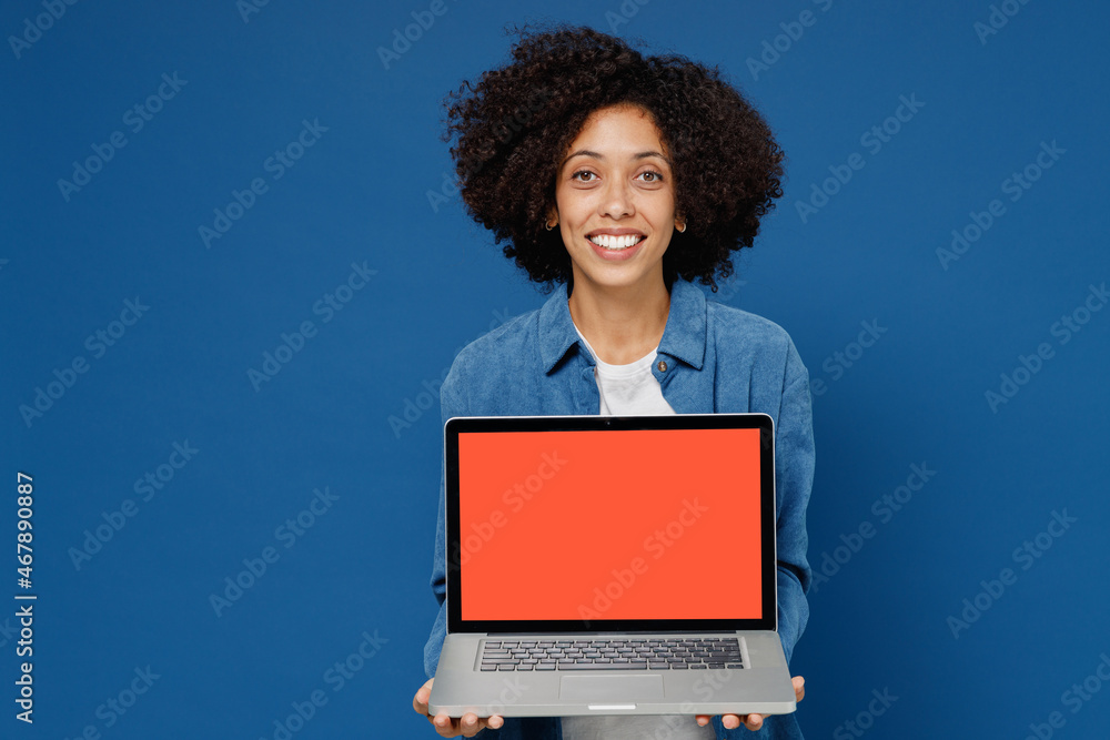 Wall mural Young black woman in casual clothes shirt white t-shirt hold use work on laptop pc computer with blank screen workspace area isolated on plain dark blue background studio. People lifestyle concept