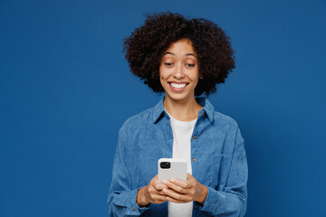 Young smiling black woman in casual clothes shirt white t-shirt hold in hand use mobile cell phone surfing internet isolated on plain dark blue background studio portrait. People lifestyle concept