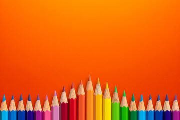 Creative background made of colour pencils on orange paper. Flat lay. Education concept.