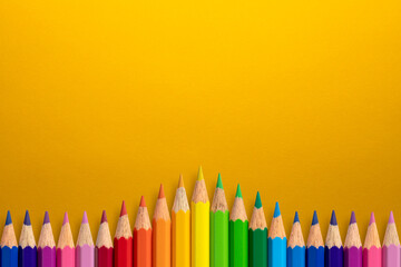 Creative background made of colour pencils on yellow paper. Flat lay. Education concept.