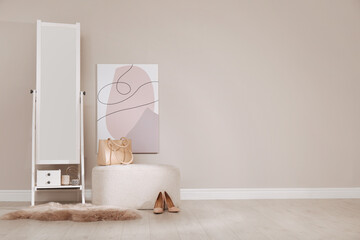 Stylish pouf and mirror near beige wall indoors. Space for text
