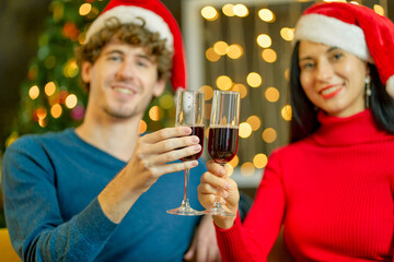 Man on blue shirt and woman on red dress celebrating with glass of wine in home christmas party