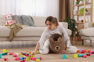 Tired young mother sitting on floor in messy living room