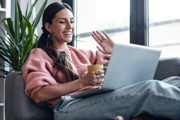 Cute woman having videocall with friends on laptop sitting on the couch at home.