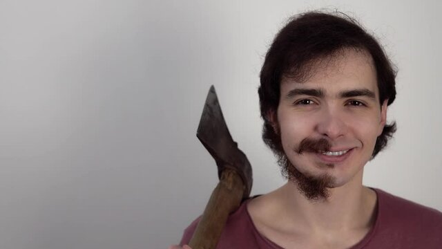 Portrait of smiling man showing that behind the axe which he holds he has not shaven all beard. Funny guy with trimmed part of his face. Person has one smooth cheek and a piece of mustache on another.