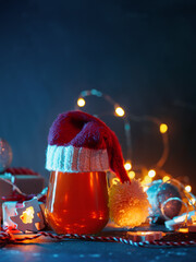 A glass of Craft Christmas beer in a Santa Claus hat. Gift boxes, glowing yellow garland, vertical photo copy space - obrazy, fototapety, plakaty