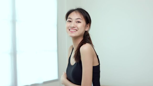 Young beautiful asian woman standing pose smiling to camera. Cheerfully sporty female workout and exercise wearing sport wear at home. Charming woman fitness training and stretching in living room