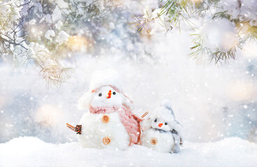 Christmas and new year snow concept with two cute snowmen in hats and scarves in snowdrift on gray background