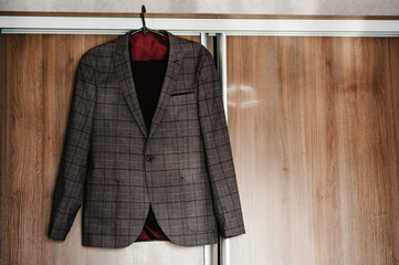 A man's jacket, brown suit with on a hanger on the background wooden wall in the room.