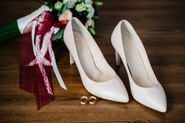 Wedding accessory bride. Stylish lacquered beige shoes, gold rings, flowers are isolated on table...