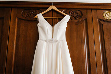 Fashionable beautiful classic lace silk wedding dress hanging on hanger in hotel wooden room. morning preparation wedding concept.