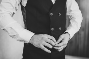 Obraz premium Man is buttoning his vest. close-up. Perfect to the last detail. Modern businessman. Fashion shot of a handsome young man in elegant classic suit. Men's beauty, fashion. Black and white photo.