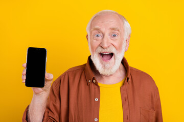 Photo of excited crazy retired man hold phone empty space screen wear brown shirt isolated yellow...