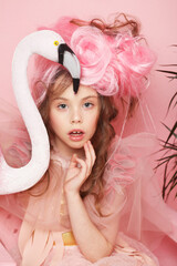 Beautiful little princess girl in pink dress with bright make-up holding a flamingo