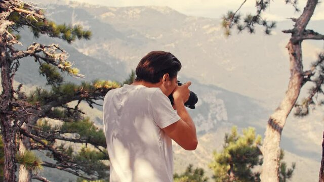 Young man photographer in white shirt taking pictures of nature on camera